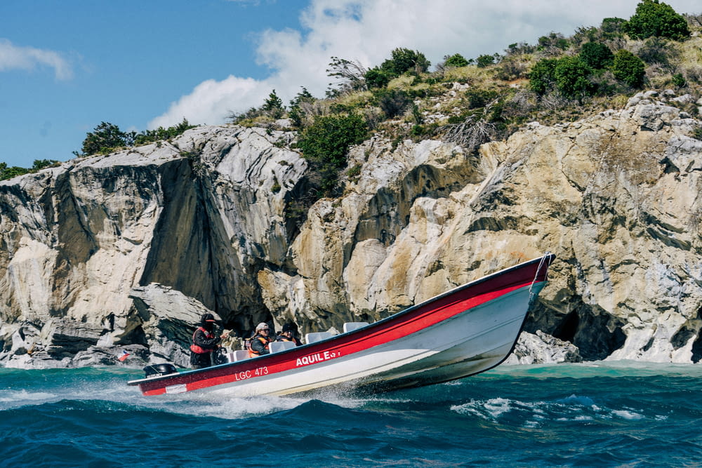 a red and white boat traveling past a rocky cliff