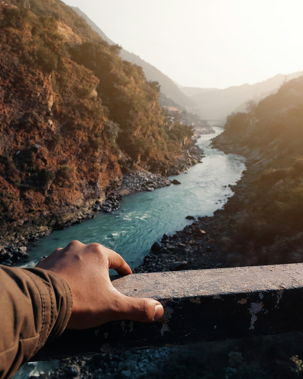 Die Hand einer Person auf einem Geländer mit Blick auf einen Fluss