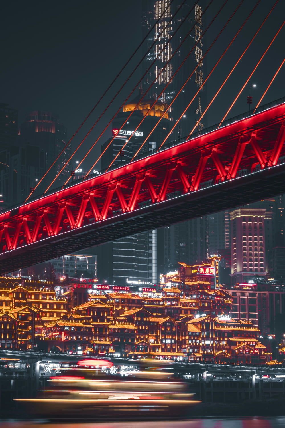 a red bridge over a river with a city in the background