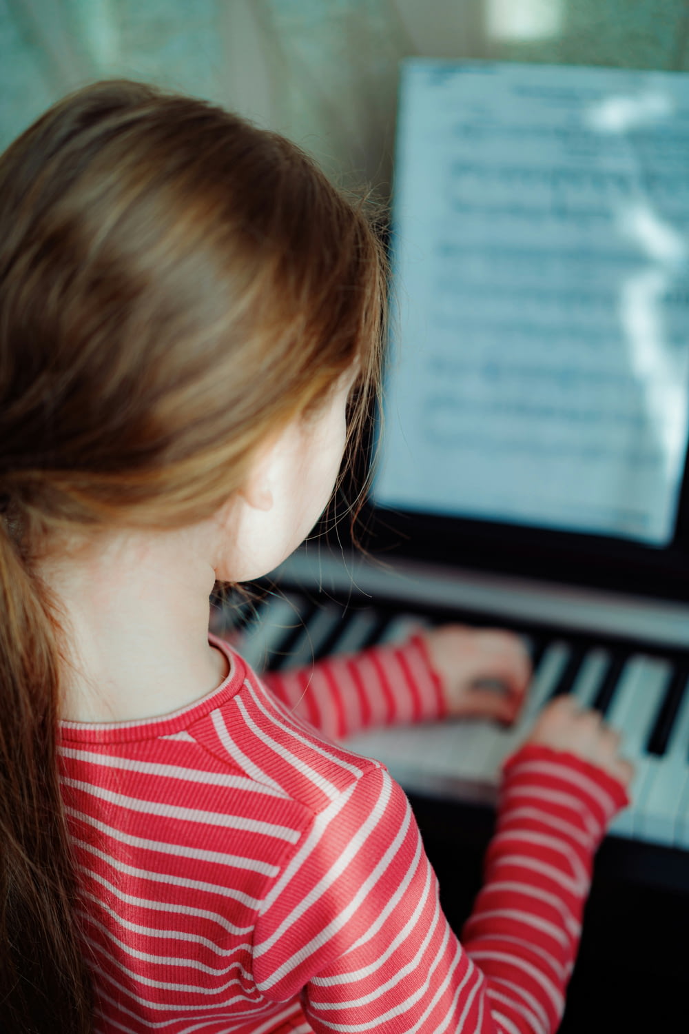 a little girl playing a piano with a sheet of music behind her