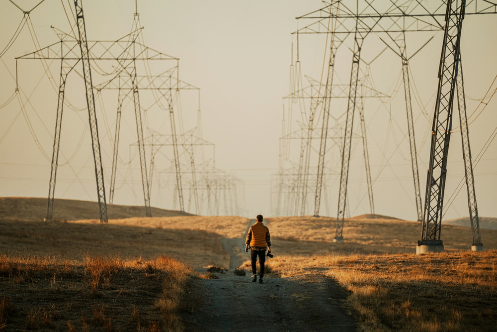 a man walking down a dirt road next to power lines