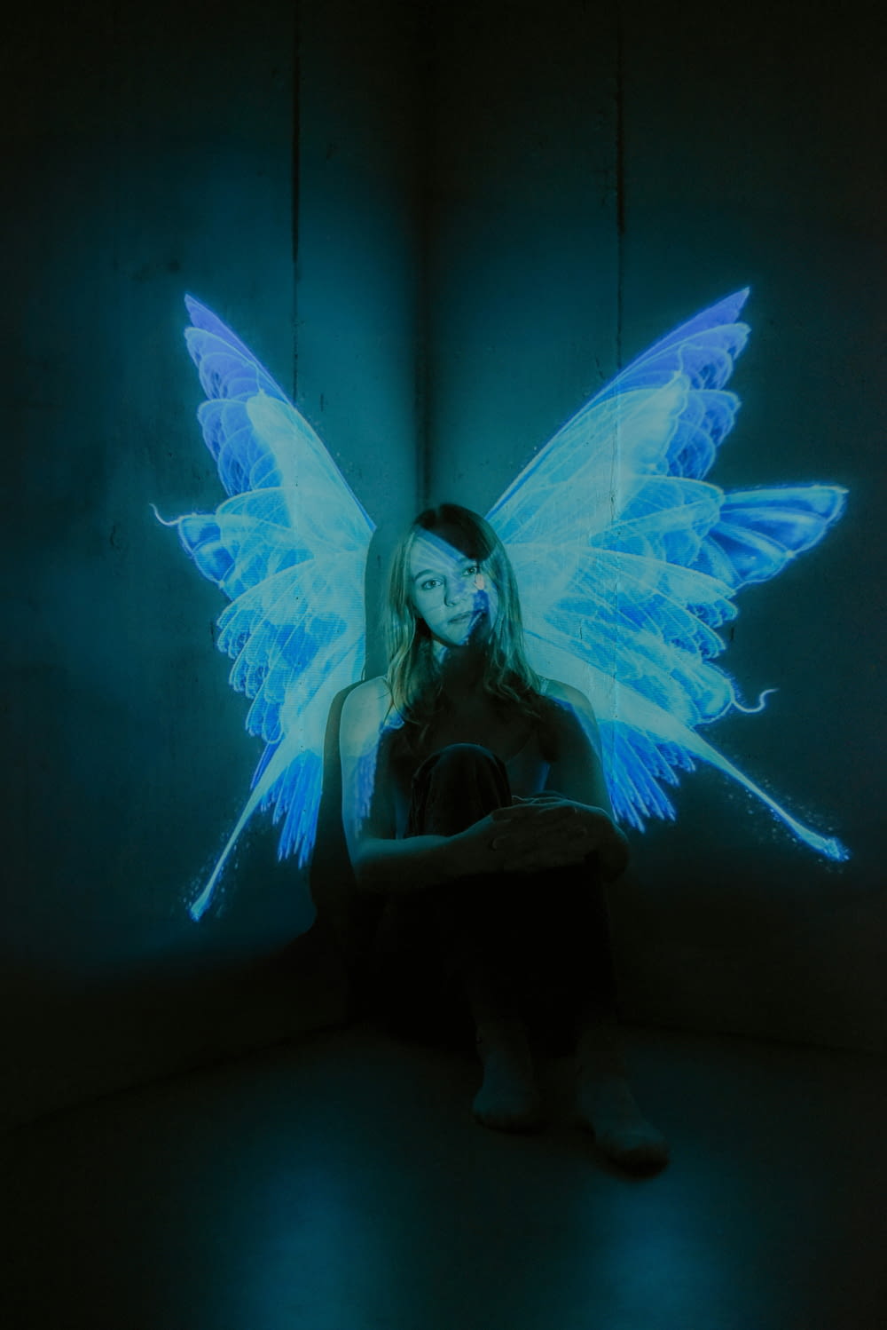 a woman sitting in a dark room with a glowing butterfly on her back