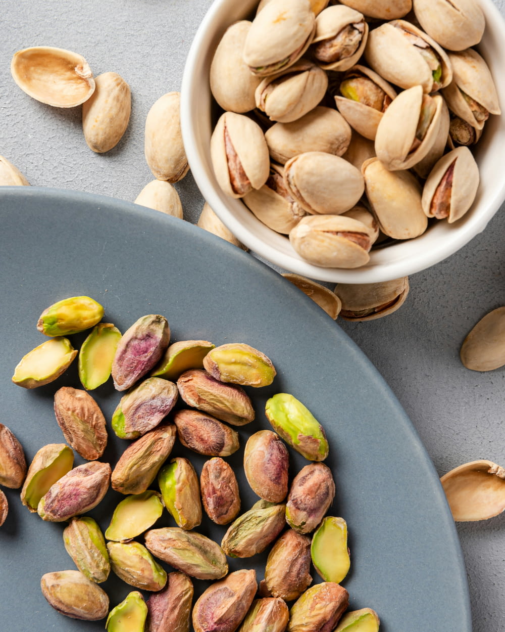 a bowl of pistachio nuts next to a plate of pistachio nuts
