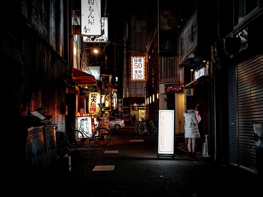 a dark alley with signs and a woman in a white dress