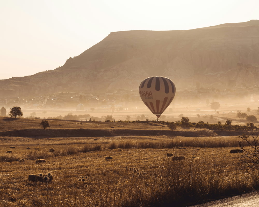 a hot air balloon flying over a dry grass field