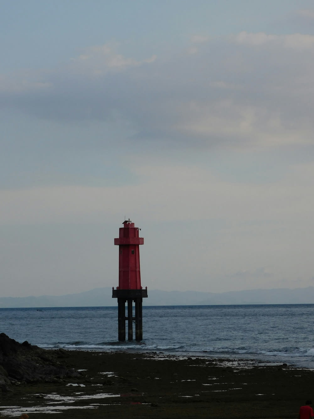 a red light house sitting on top of a sandy beach