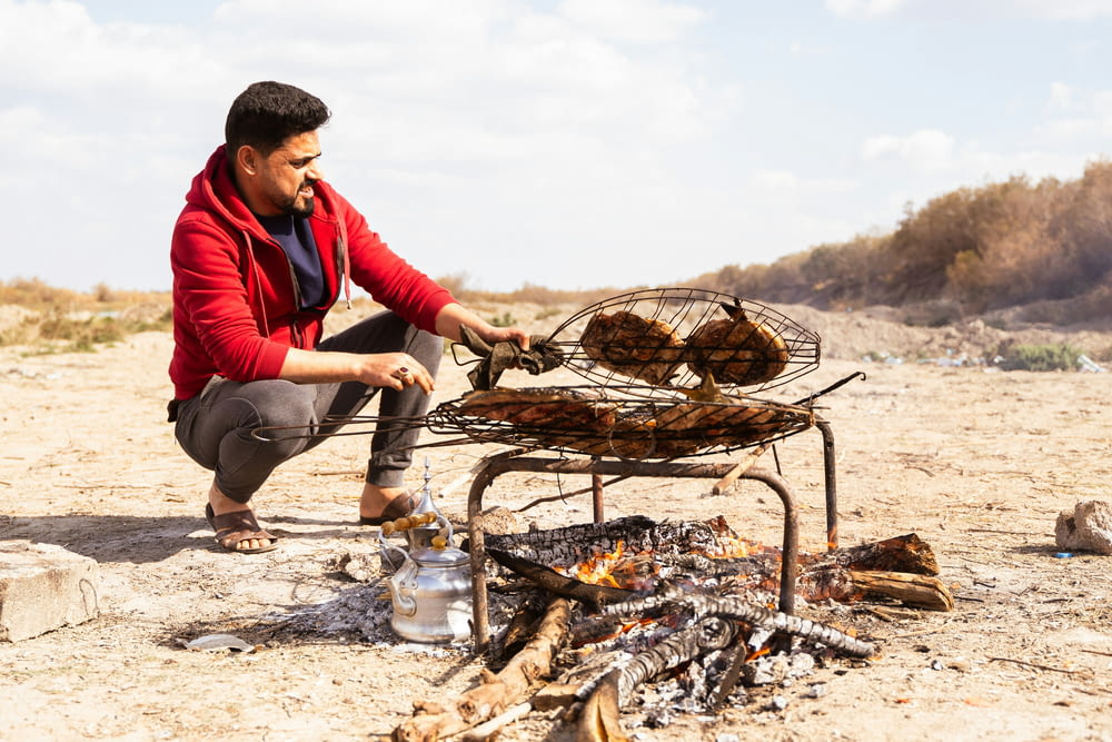a man cooking food over a fire in the desert