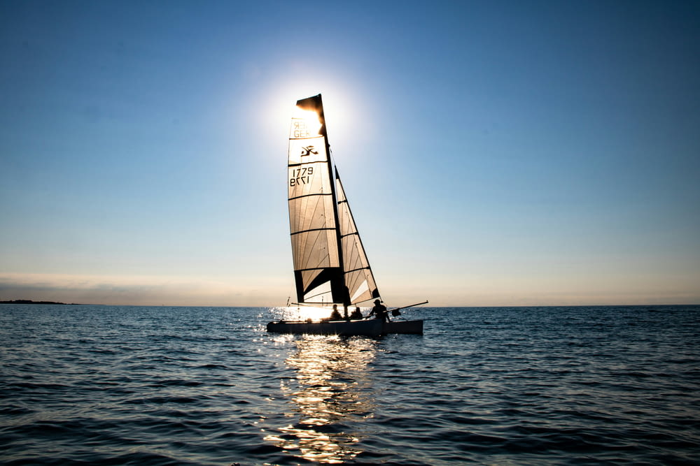 a sailboat sailing on the water with the sun in the background