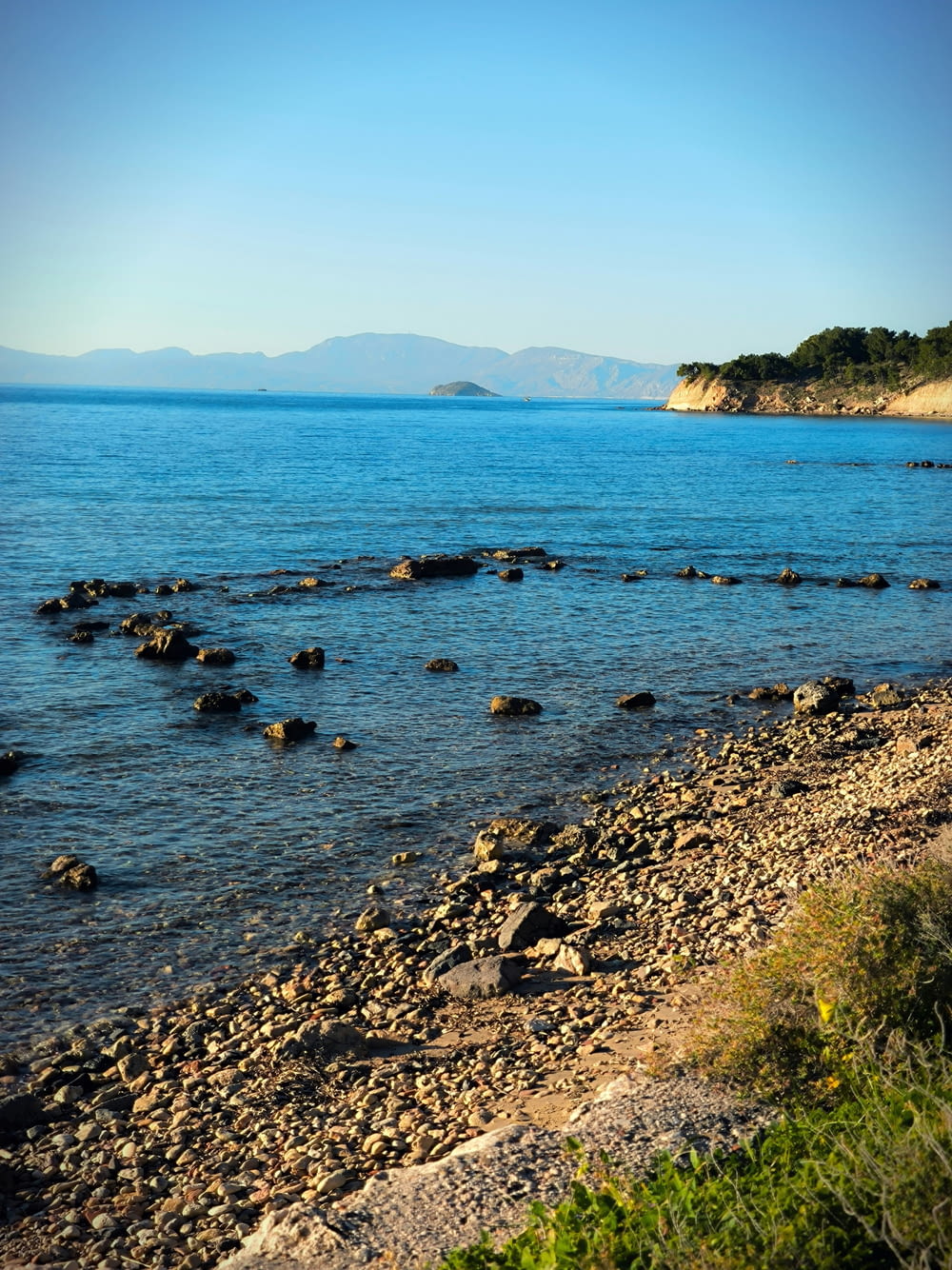 a rocky shore line with a body of water and mountains in the distance
