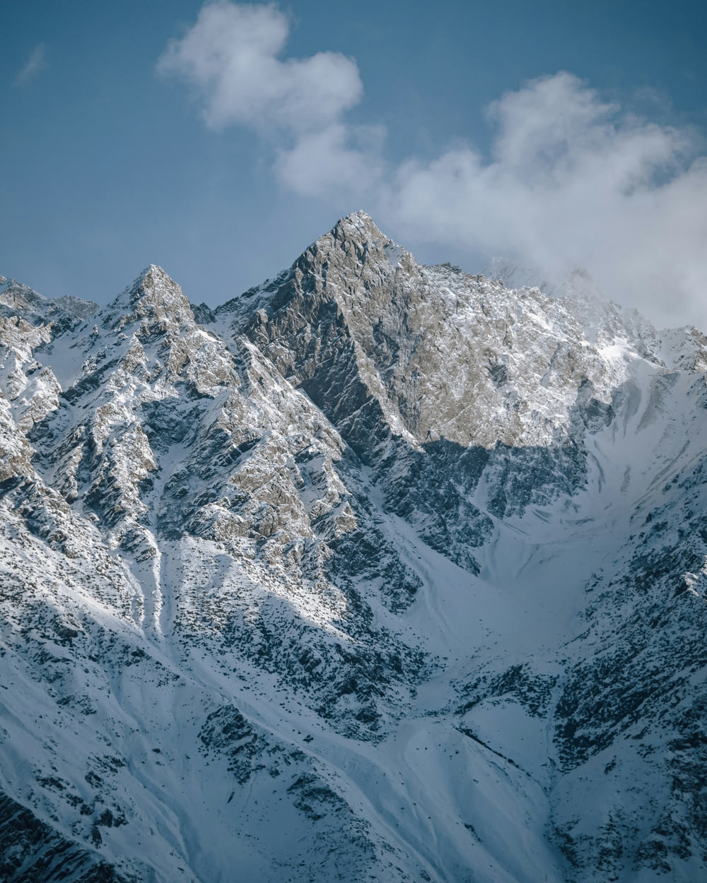 a snow covered mountain range under a cloudy blue sky