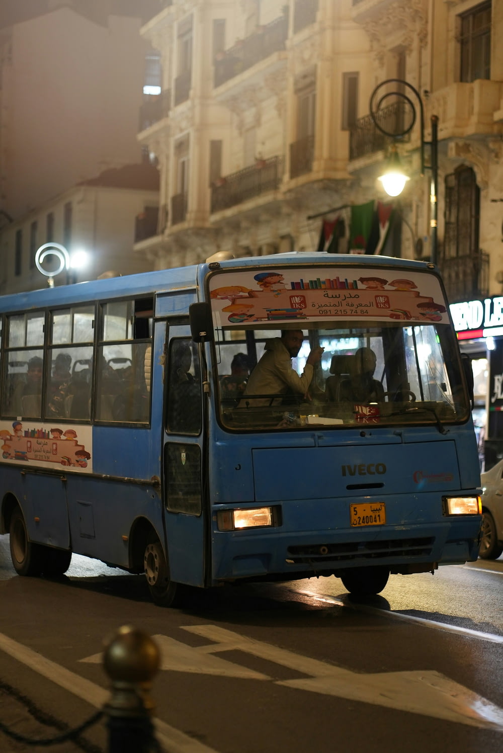 a blue bus driving down a street next to tall buildings