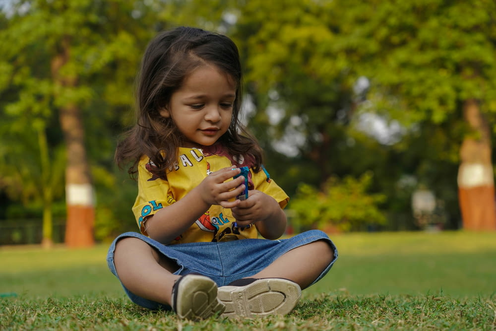 a little girl sitting on the grass playing with a cell phone