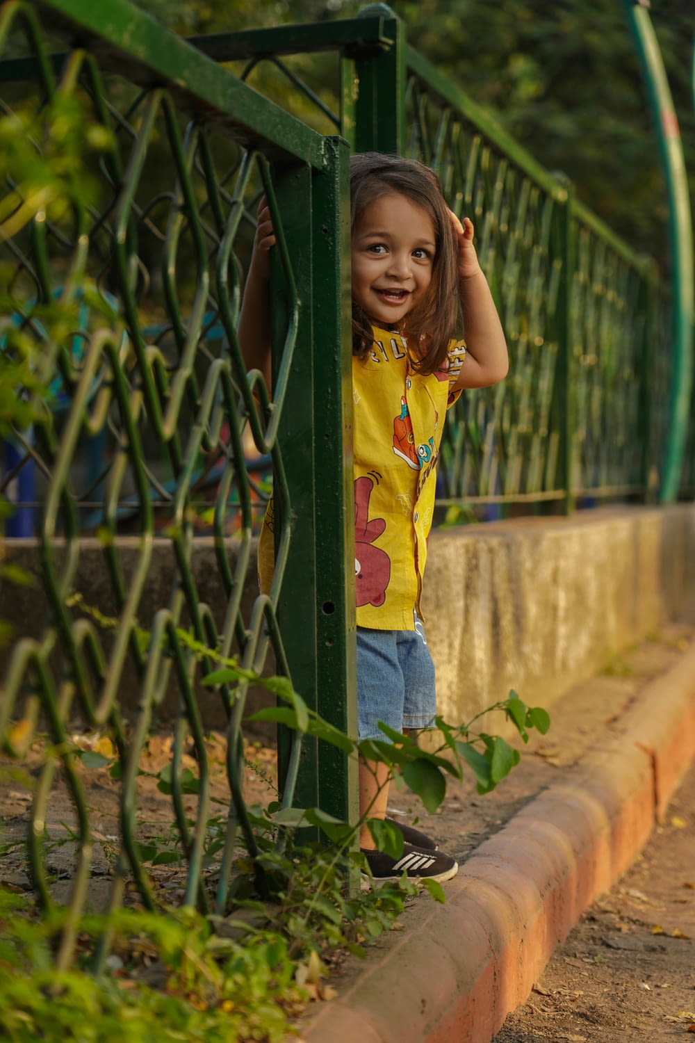 a little girl standing next to a green fence