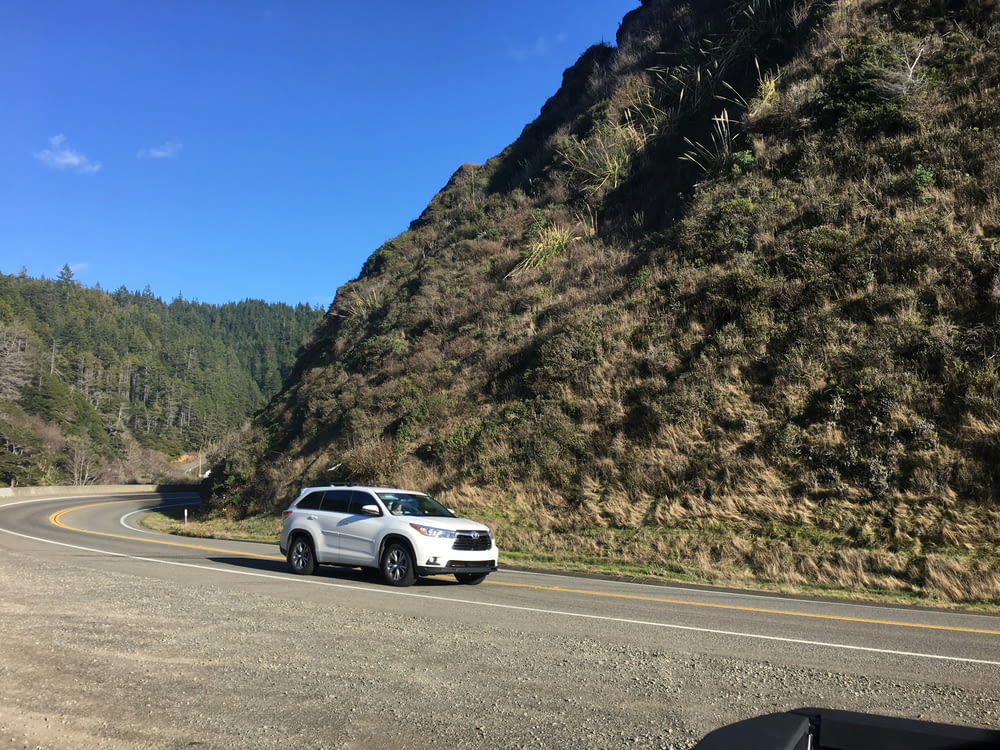 a white car driving down a curvy road next to a mountain