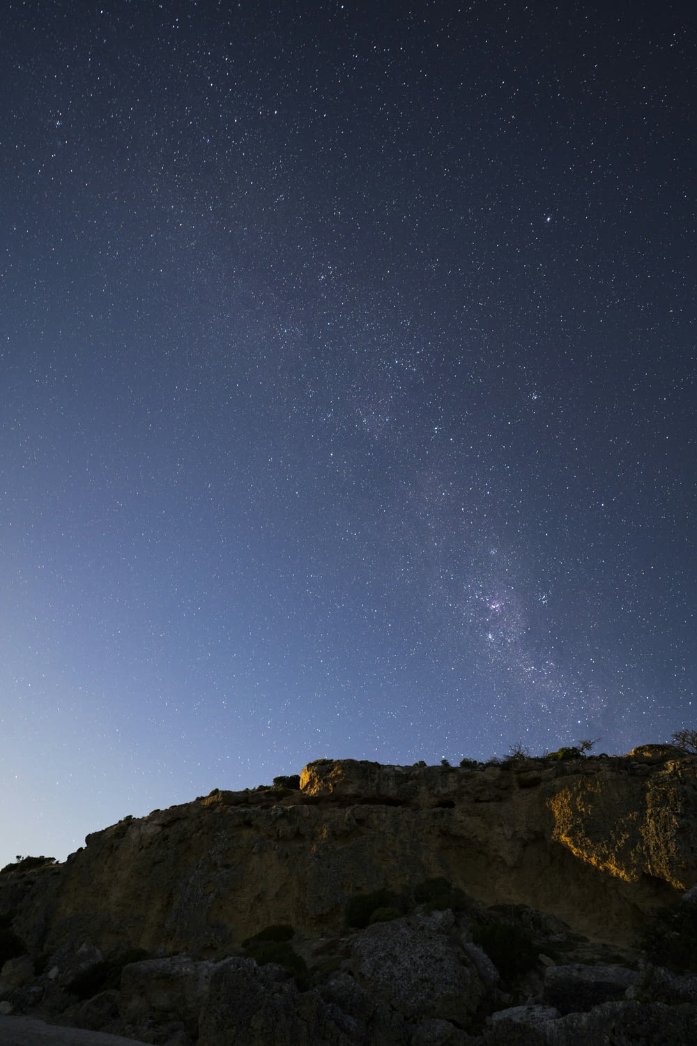 the night sky with stars above a rocky hill