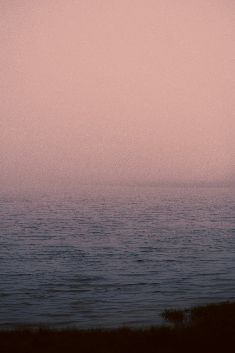 a large body of water sitting under a pink sky