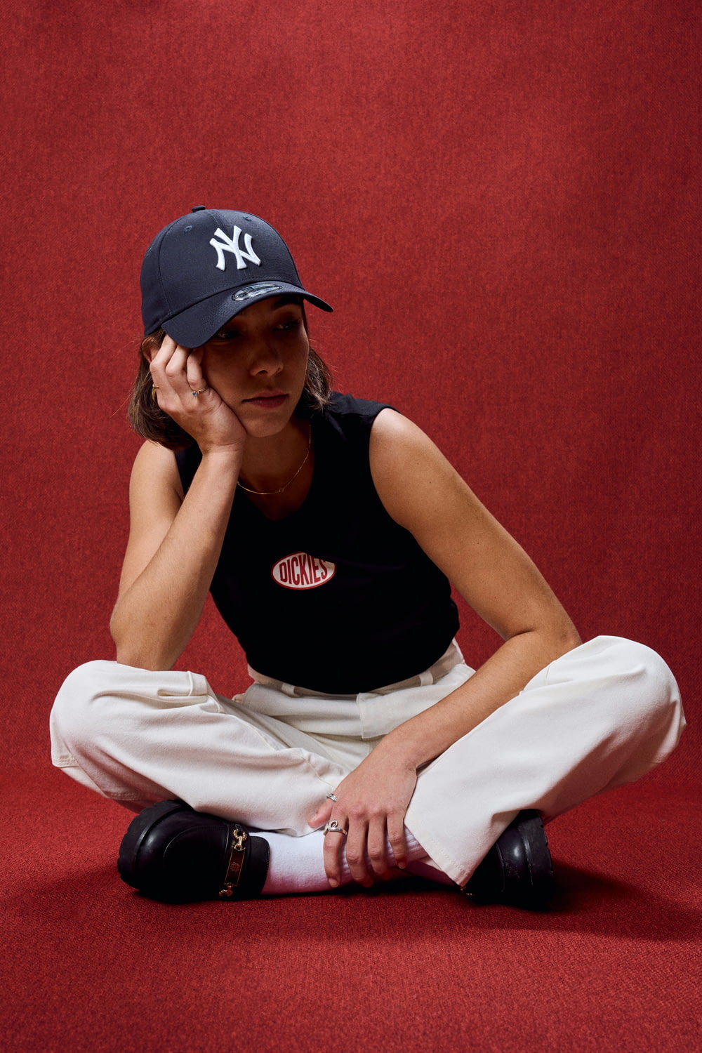 a woman sitting on the ground wearing a new york yankees hat