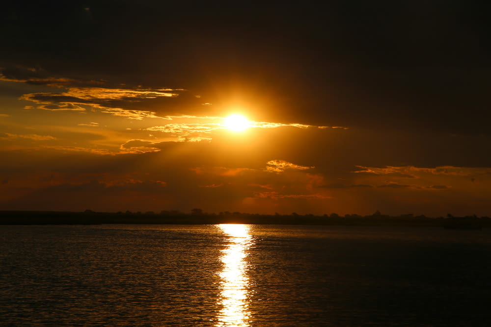 a large body of water with a sun setting in the background