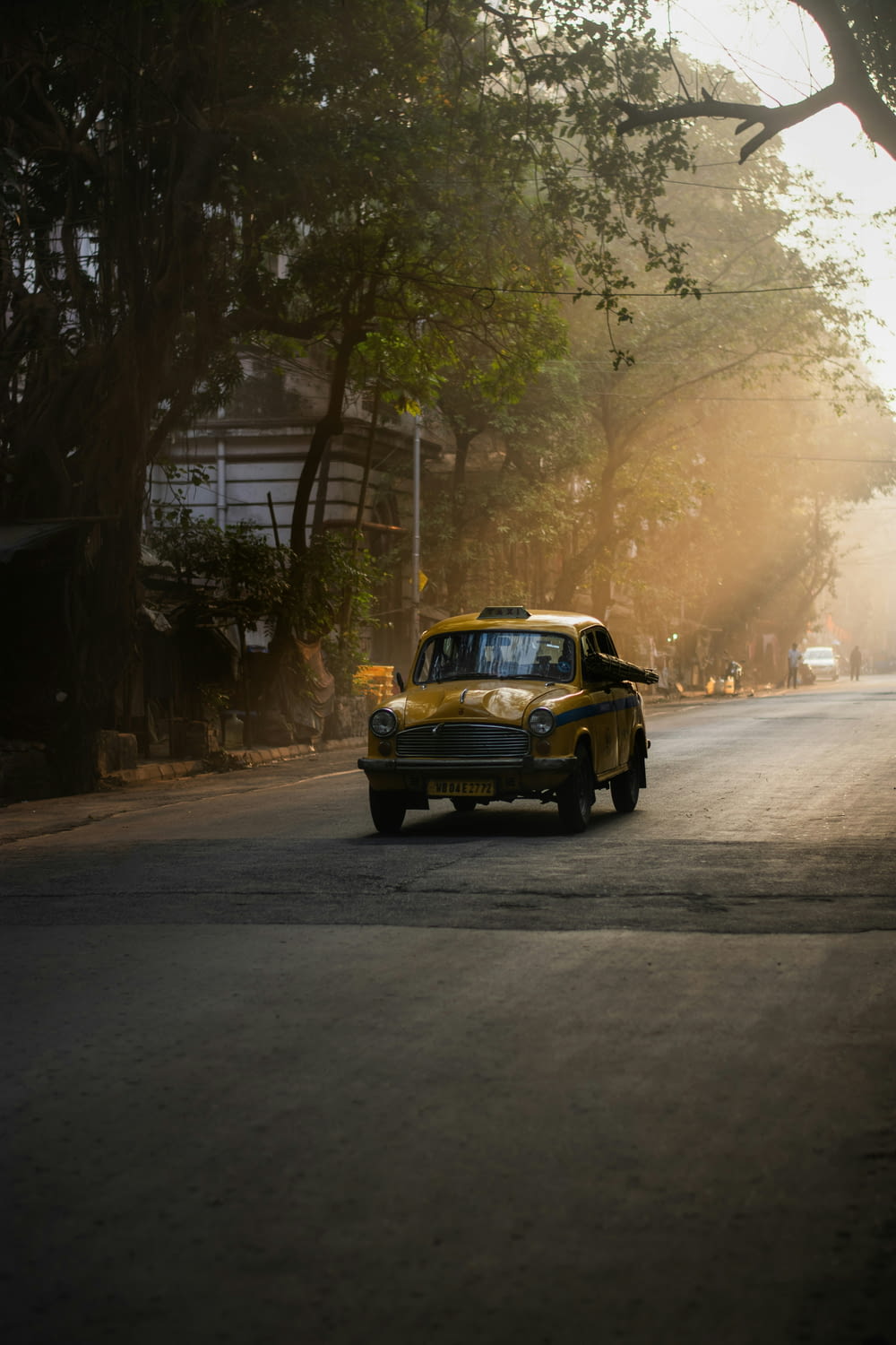 a yellow car driving down a street next to trees