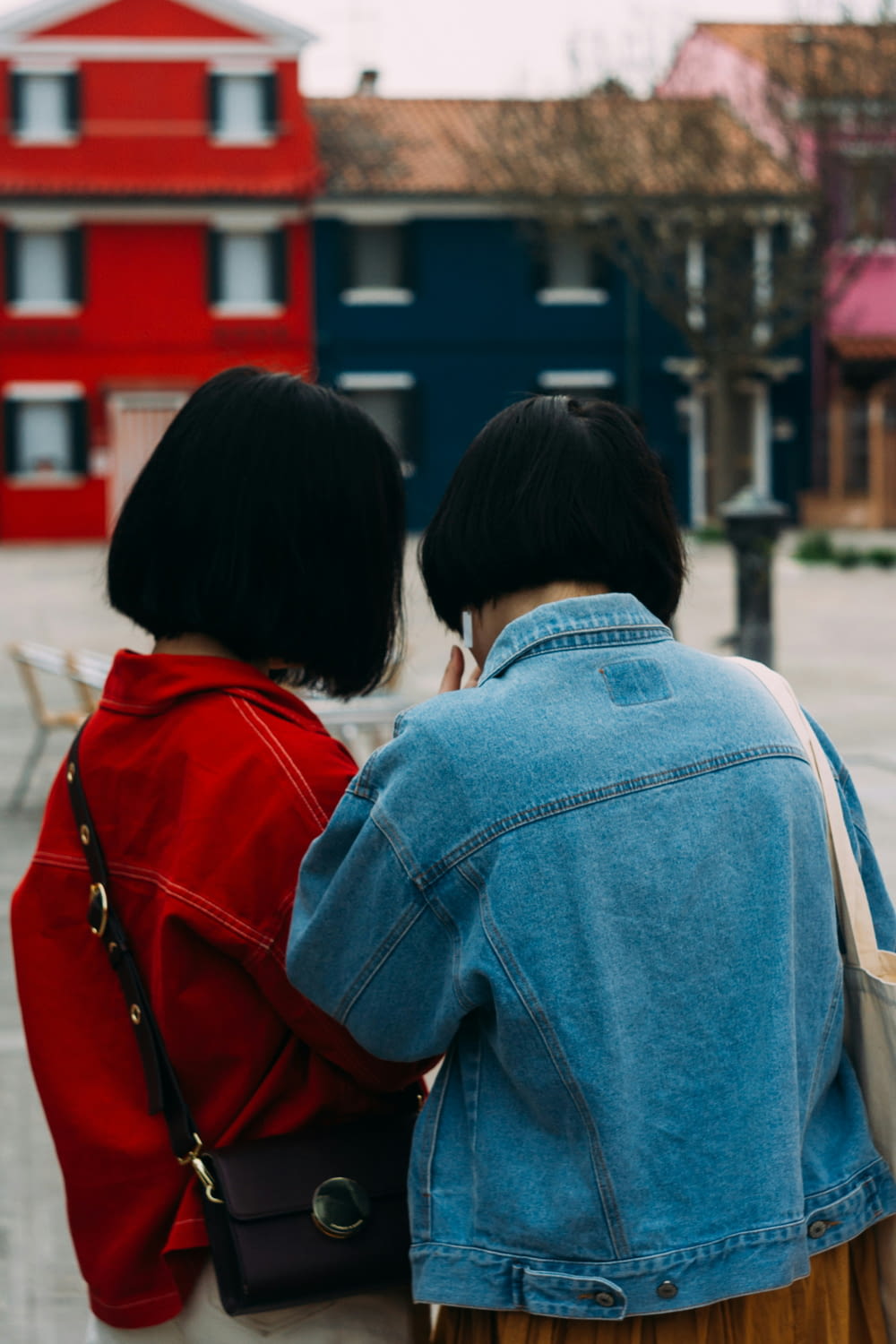 two women walking down a street with a red building in the background