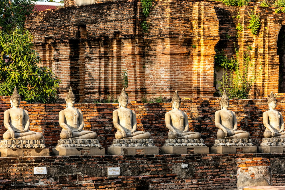 a row of buddha statues sitting on top of a stone wall