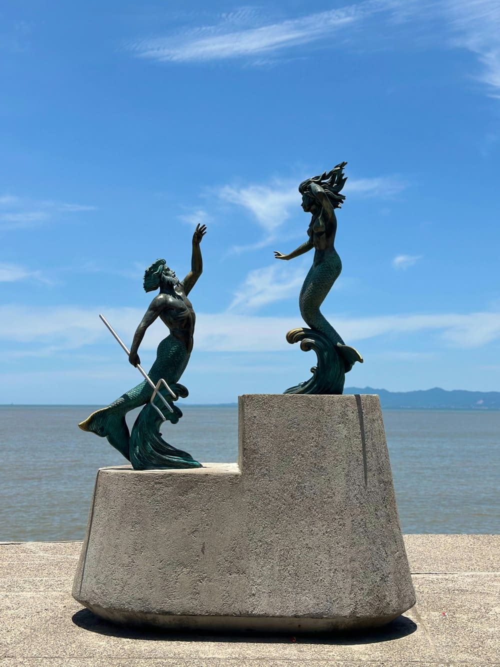 a statue of two mermaids on a rock near the ocean