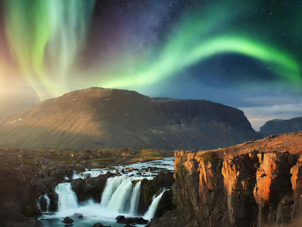 a waterfall with a green and purple aurora light above it