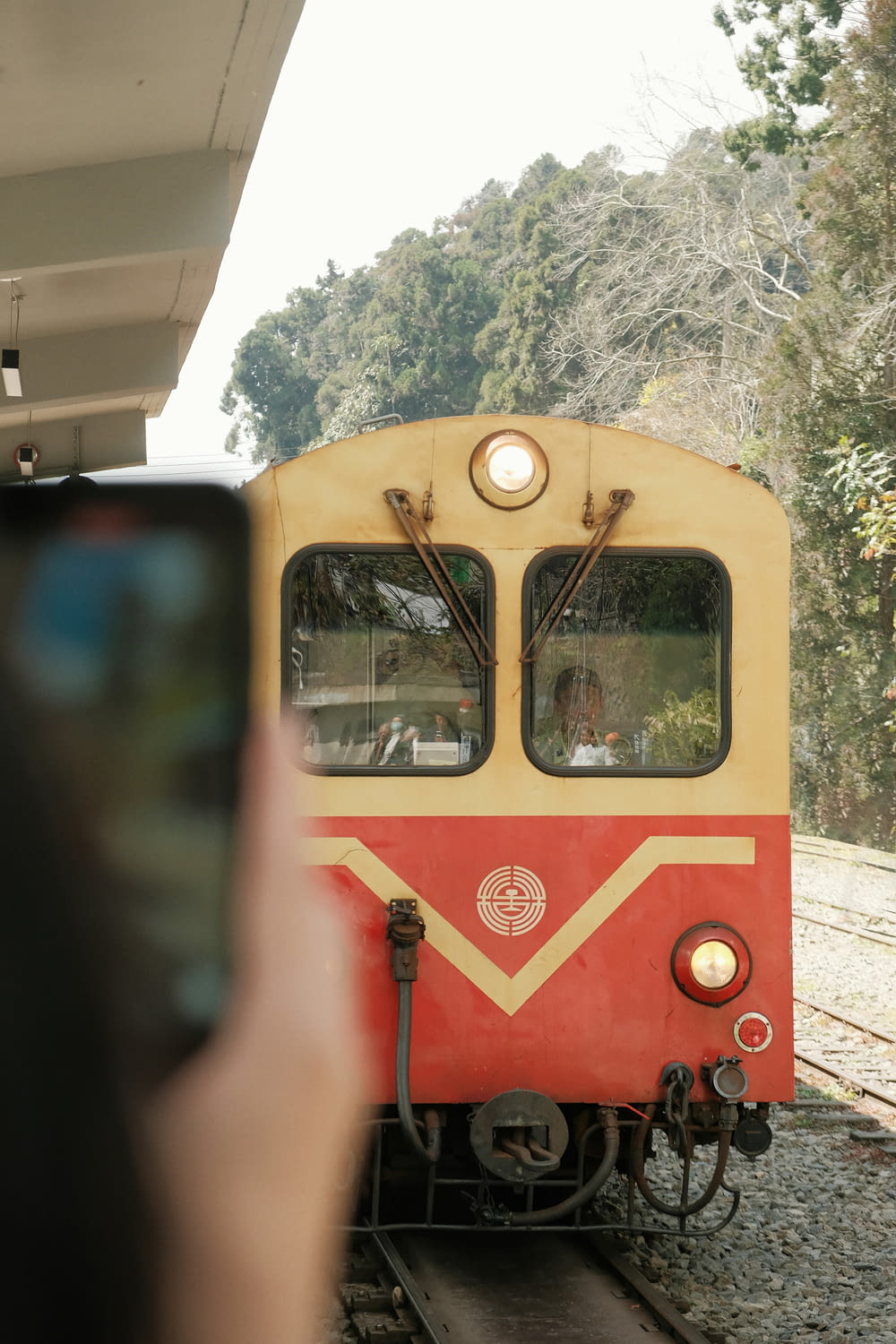 a person taking a picture of a red and yellow train