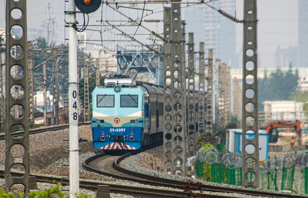a blue train traveling down train tracks next to tall buildings