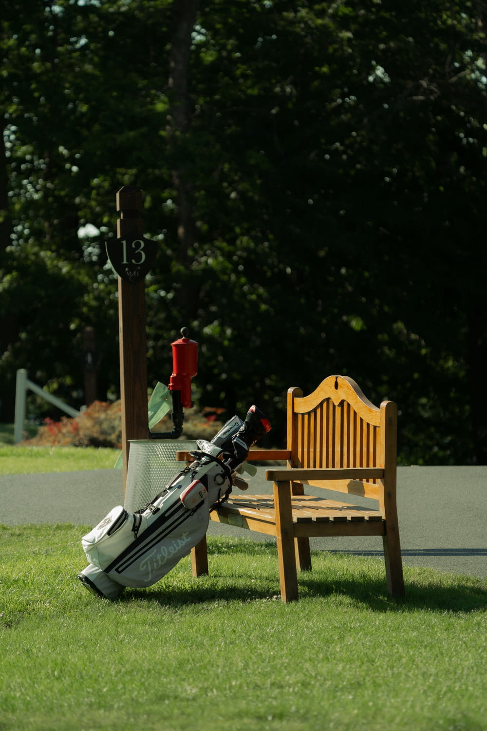 a wooden bench sitting in the grass next to a golf bag