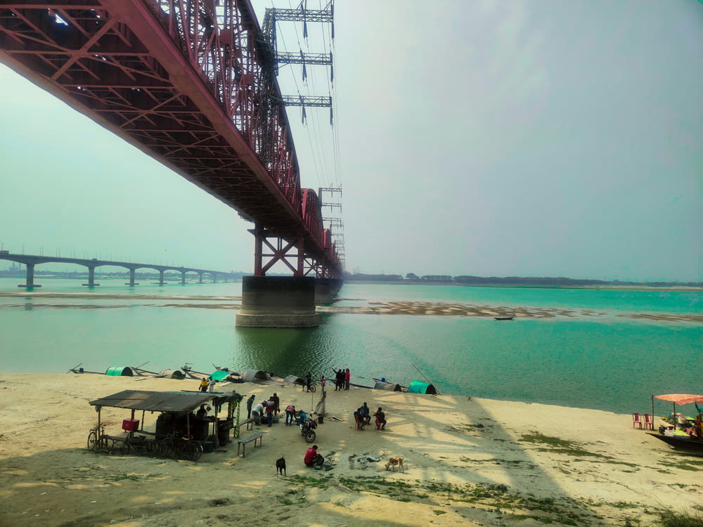 a group of people standing on a beach under a bridge