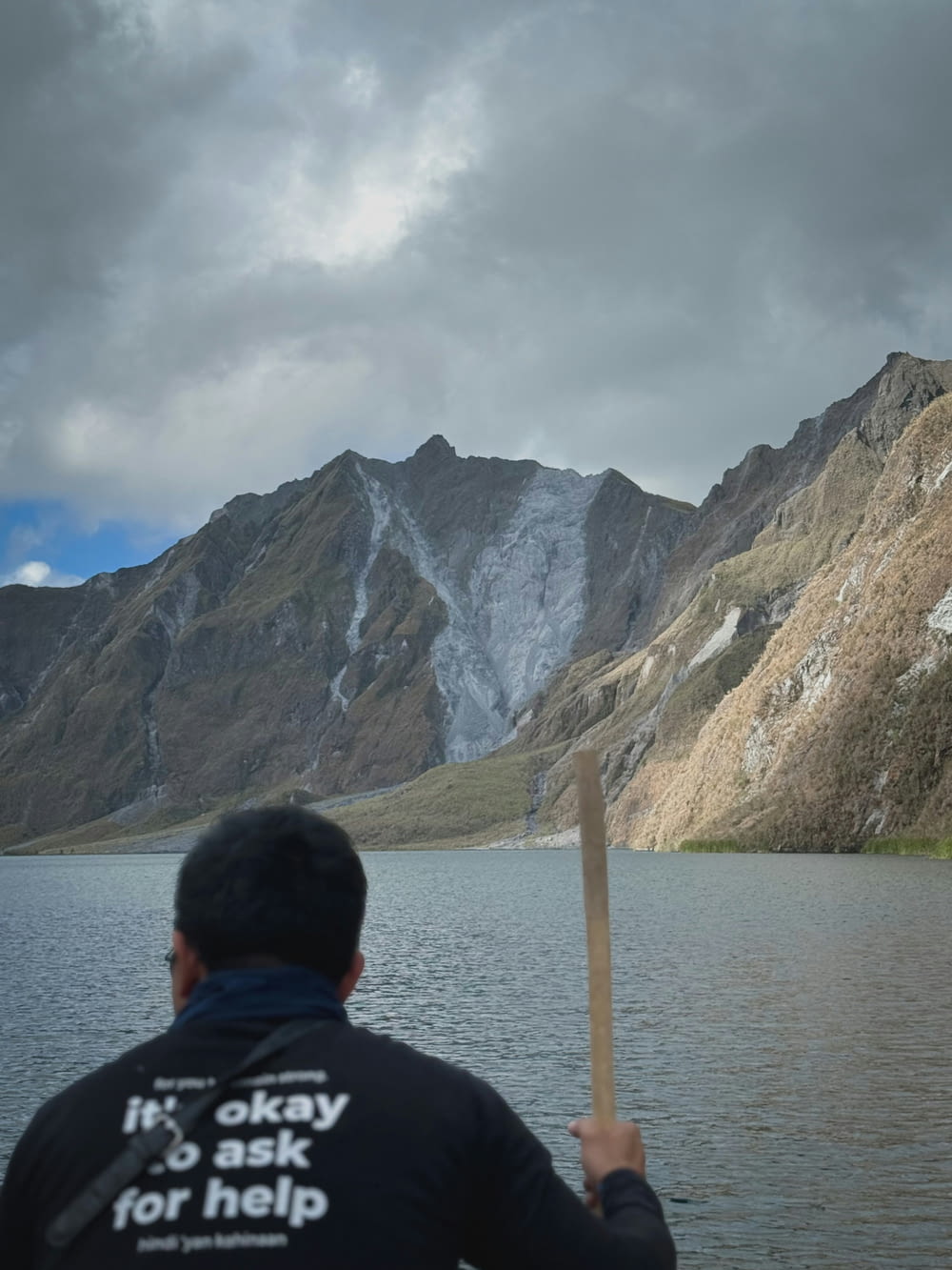 a man holding a stick in front of a mountain lake