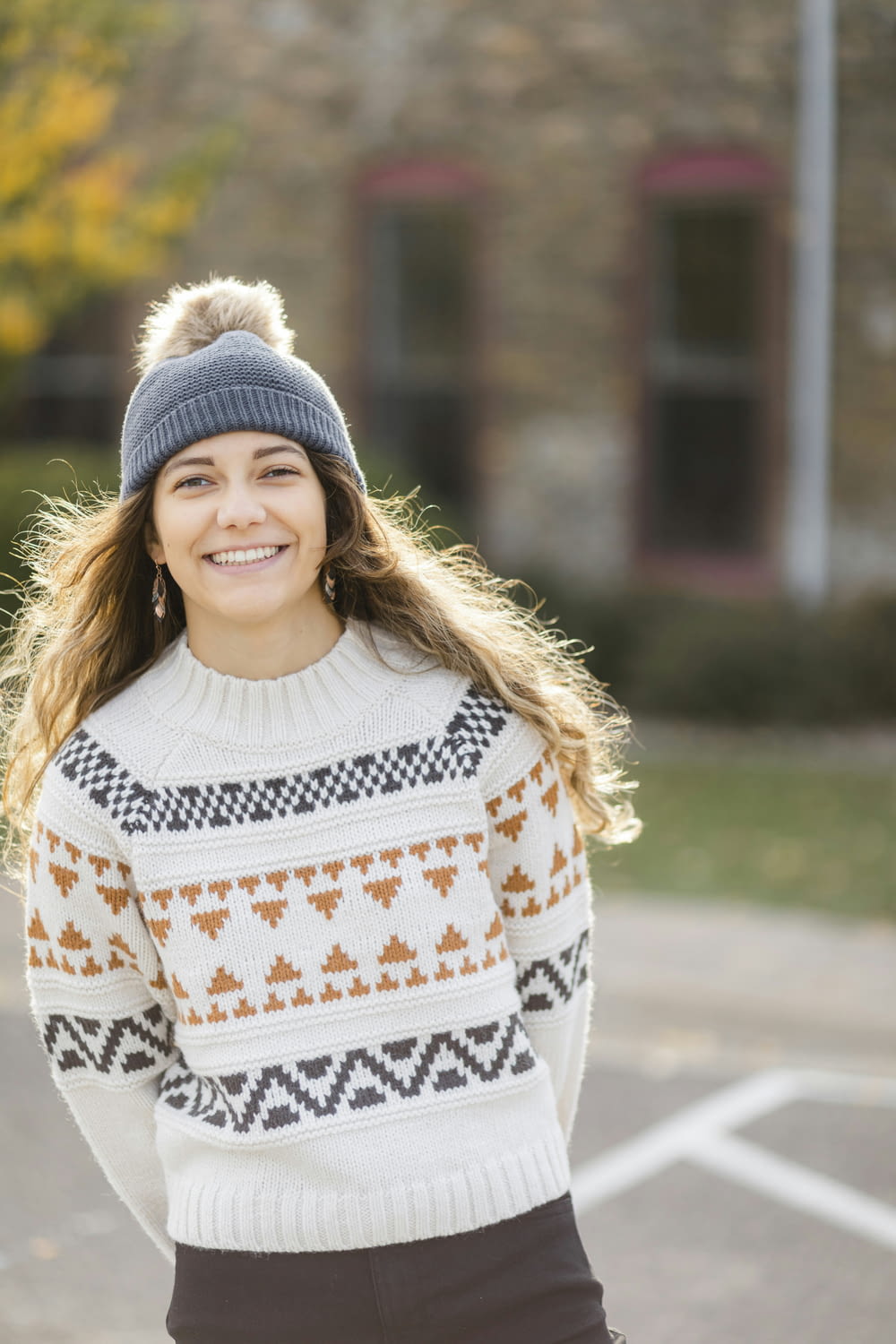 a woman standing in a parking lot wearing a sweater and a beanie
