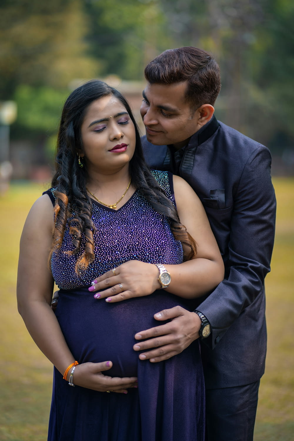 a pregnant couple cuddling in a park