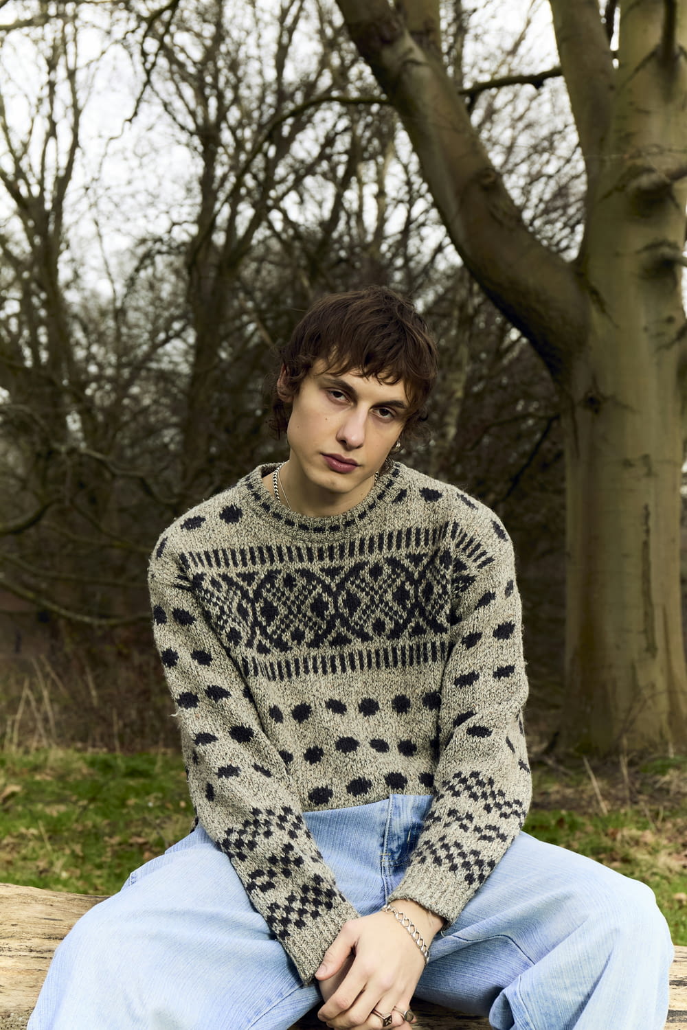 a young man sitting on a wooden bench wearing a sweater