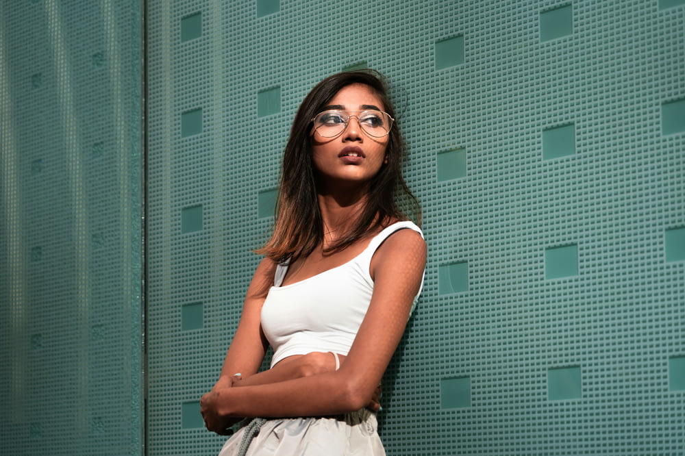 a woman wearing glasses leaning against a wall