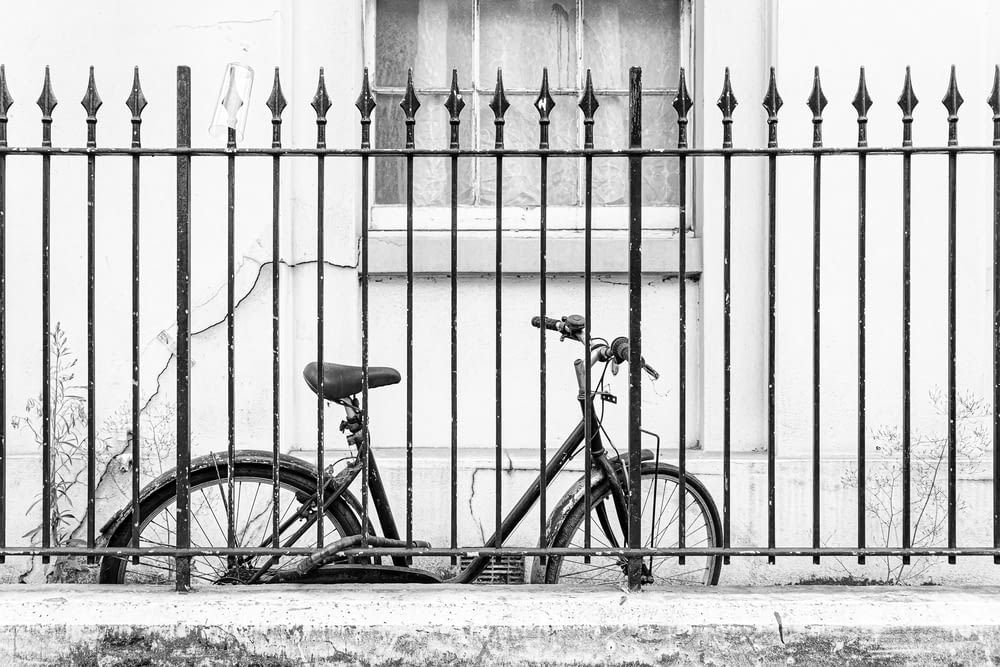 a bicycle parked next to a fence in front of a building