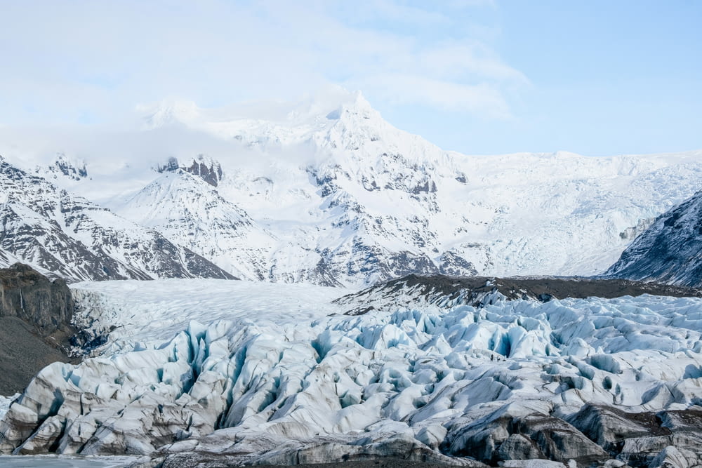 a large glacier with snow covered mountains in the background