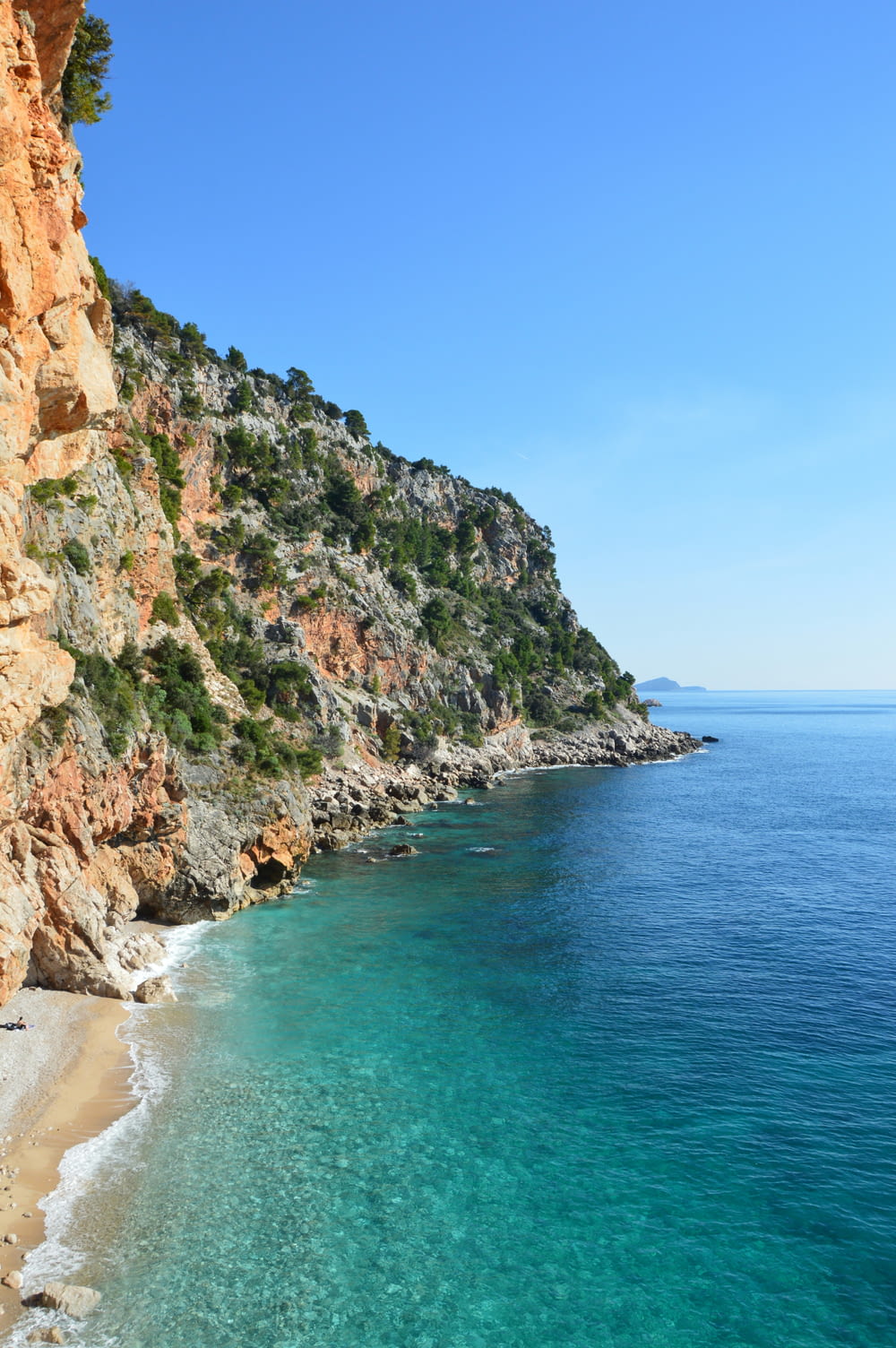 a sandy beach next to a cliff with clear blue water