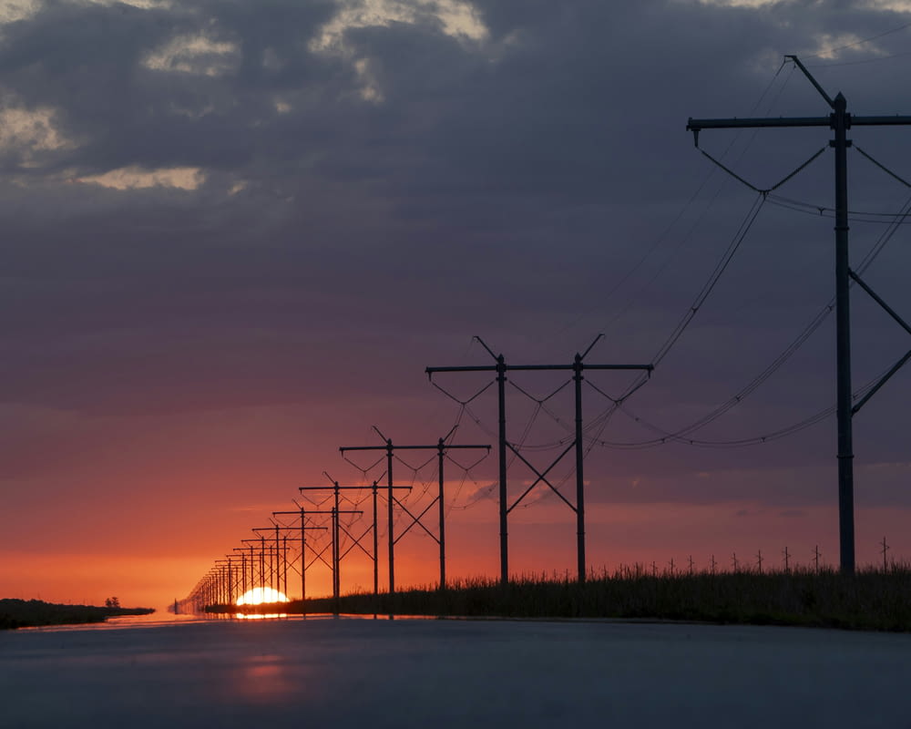 the sun is setting behind a line of power poles