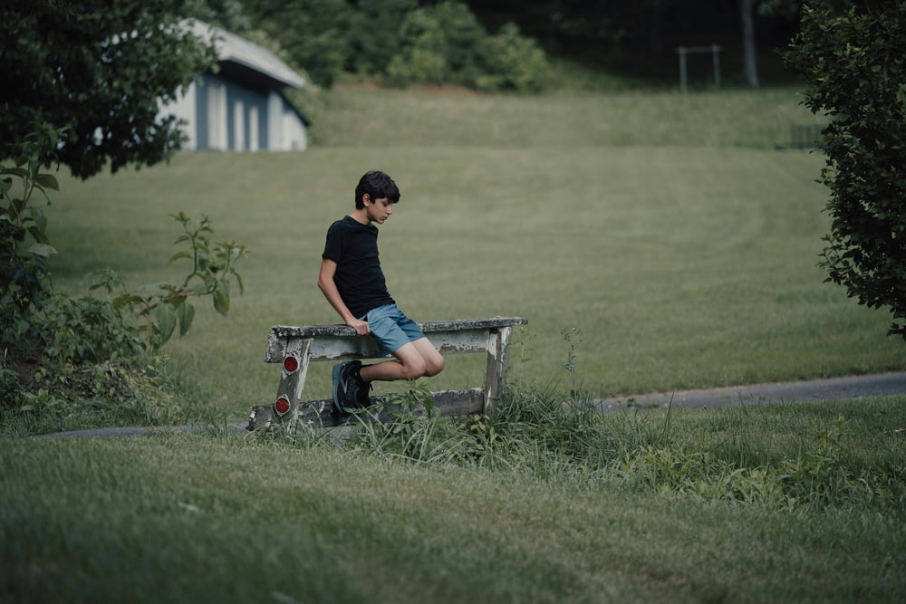 a boy sitting on a bench in a field