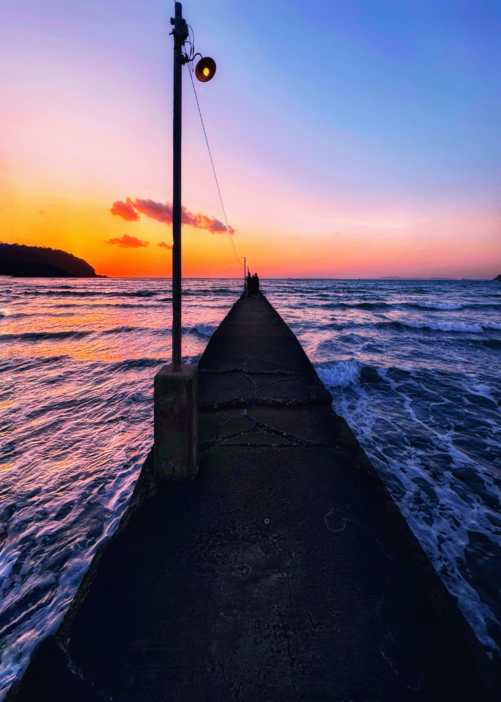a light pole sitting on the end of a pier next to the ocean