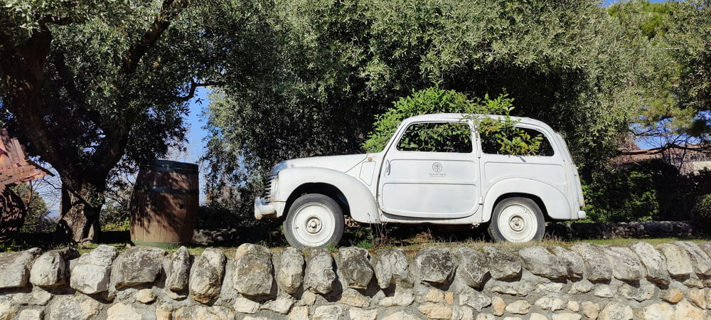 an old white car parked on a stone wall