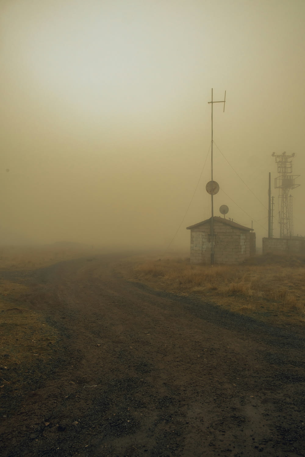 a dirt road with a house in the fog