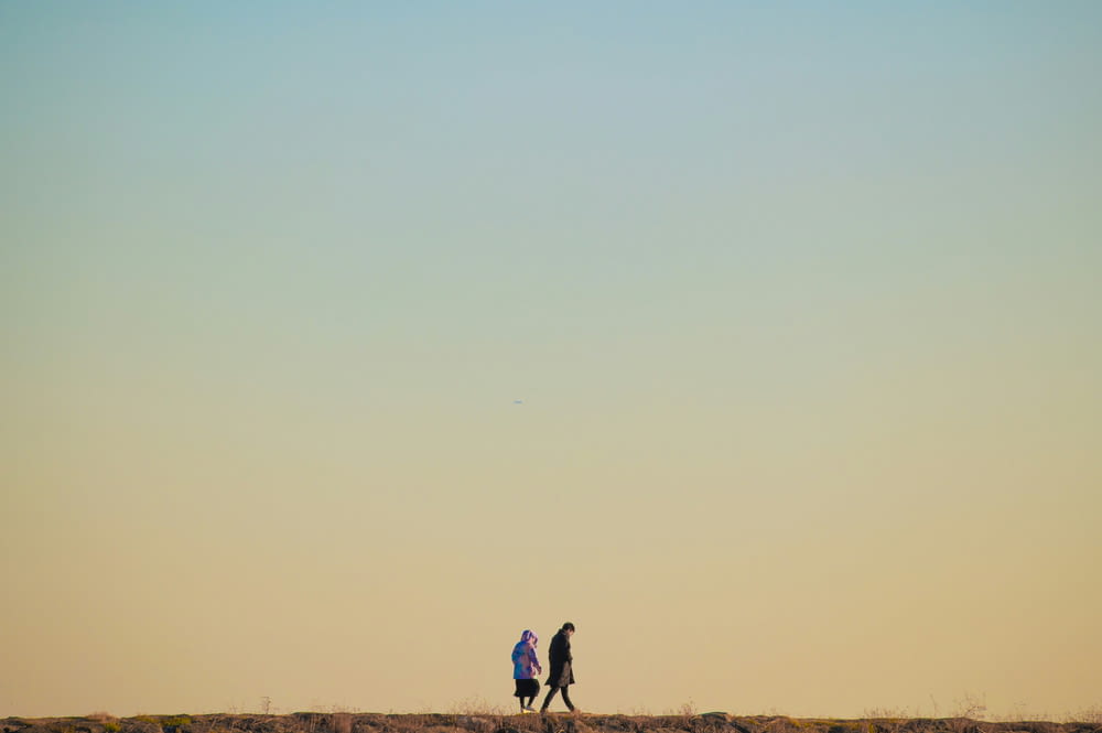 um casal de pessoas caminhando por um campo de grama seca