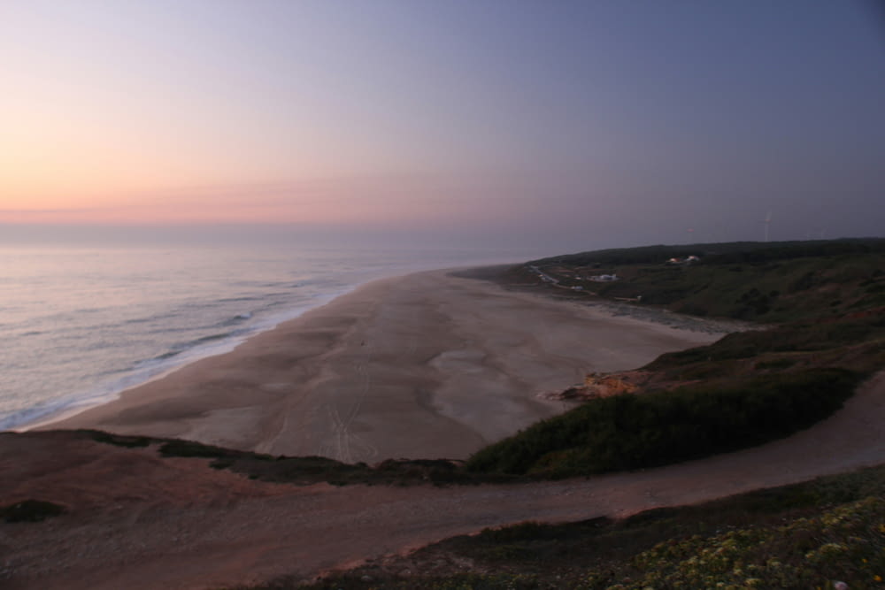 a view of a beach at sunset from a hill