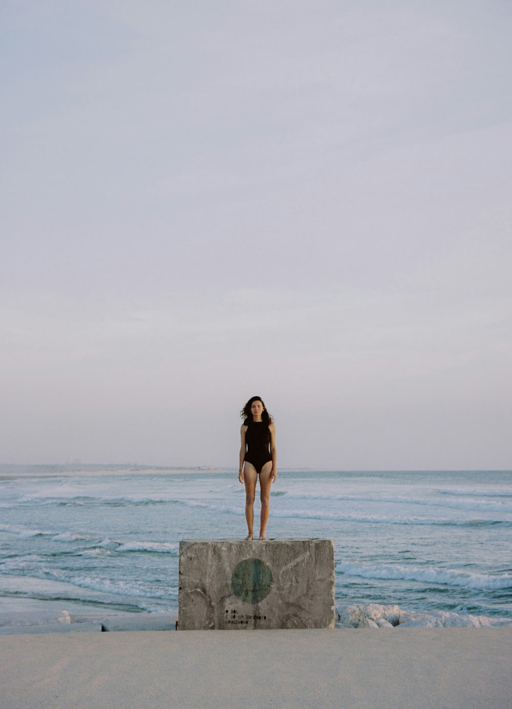 a woman standing on top of a stone block near the ocean