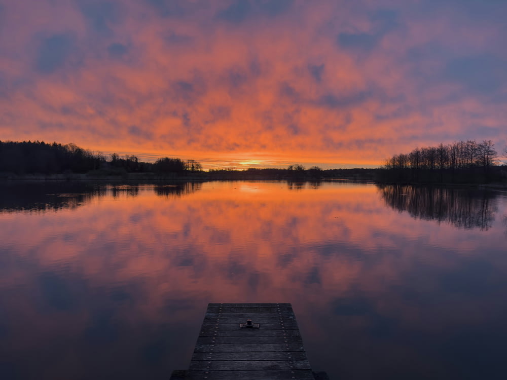 a dock sitting on top of a lake under a colorful sky