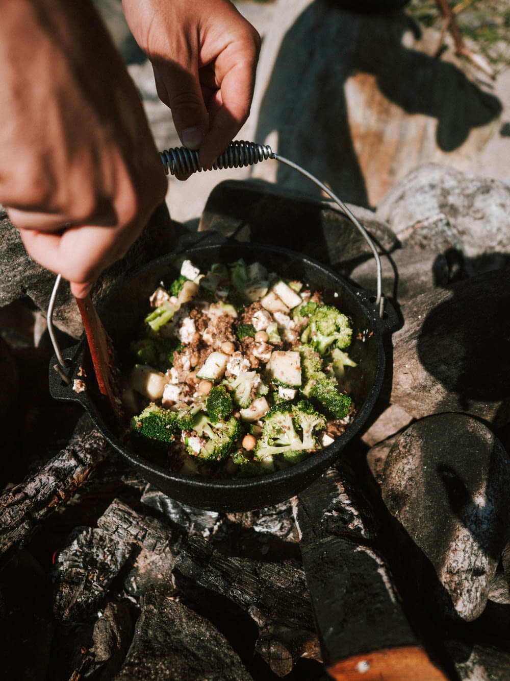 a person is cooking broccoli and other food on a campfire