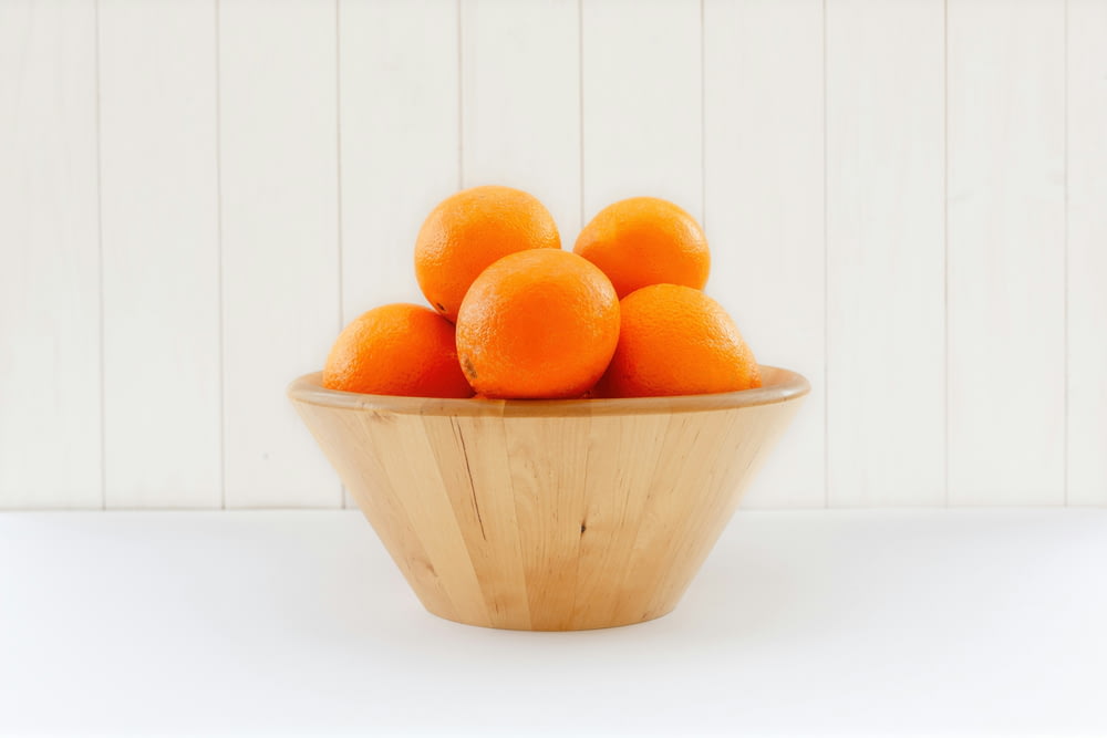 a wooden bowl filled with oranges on top of a table